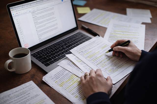 Person reviewing highlighted customer interview transcripts at a desk with a laptop during research analysis.