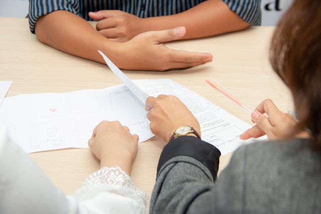 3 people sitting at a desk with papers, only the hands visible.